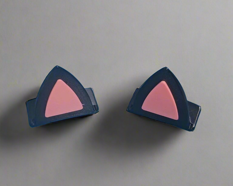A pair of black cat-ear style clips or accessories with pink triangular inner sections, shown on a plain light gray background.