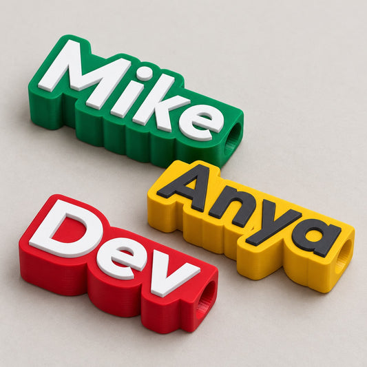 Name Tag for Pen or Straw: three tags (Mike green, Anya yellow, Dev red) laid flat in a loose fan, top-down at a slight angle