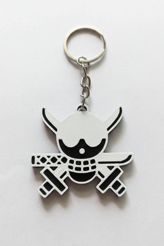 A silver metal keychain featuring a stylized skull and crossbones design with black and white details, resting on a plain light gray surface.