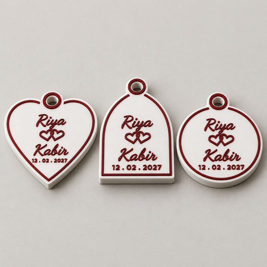 Wedding Favour Keychain: heart, Mughal arch and medallion versions side by side, laid flat, all with Riya, Kabir and the date