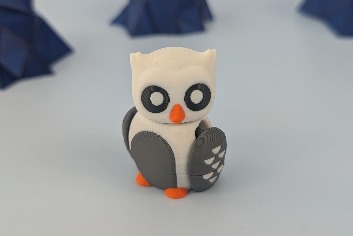 Small owl figurine with black eyes and orange beak on a white background