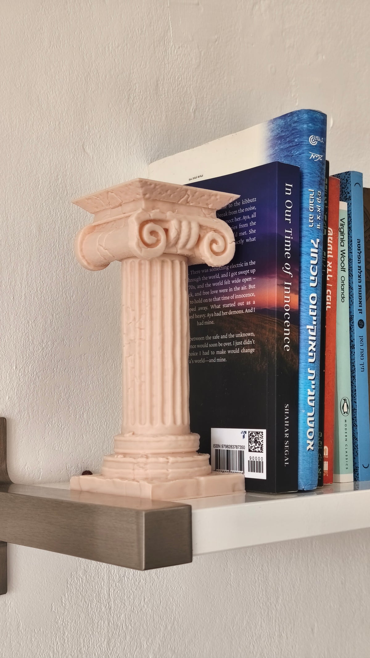 Decorative bookend shaped like a classical column on a shelf with books.