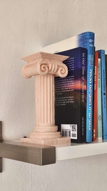Decorative bookend shaped like a classical column on a shelf with books.