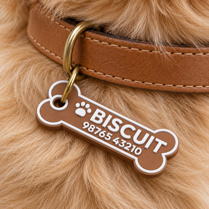 Bone Pet ID Tag: brown 'BISCUIT' tag hanging from the ring of a tan leather dog collar on a beige golden retriever's neck, close-up of the collar and fur only, no face