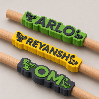 Dinosaur Name Pencil Topper: three toppers (Arlo, Reyansh, Om) each on the top of a pencil, the pencils lying side by side