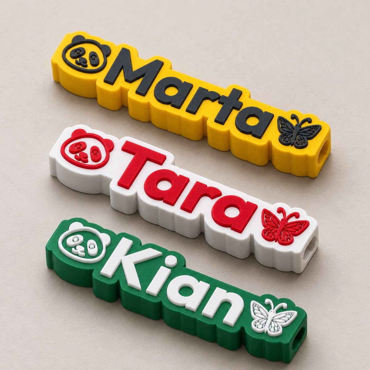 Emoji Name Pencil Topper: three toppers (Marta yellow, Tara white with red, Kian green with white) laid flat in a loose fan, top-down at a slight angle