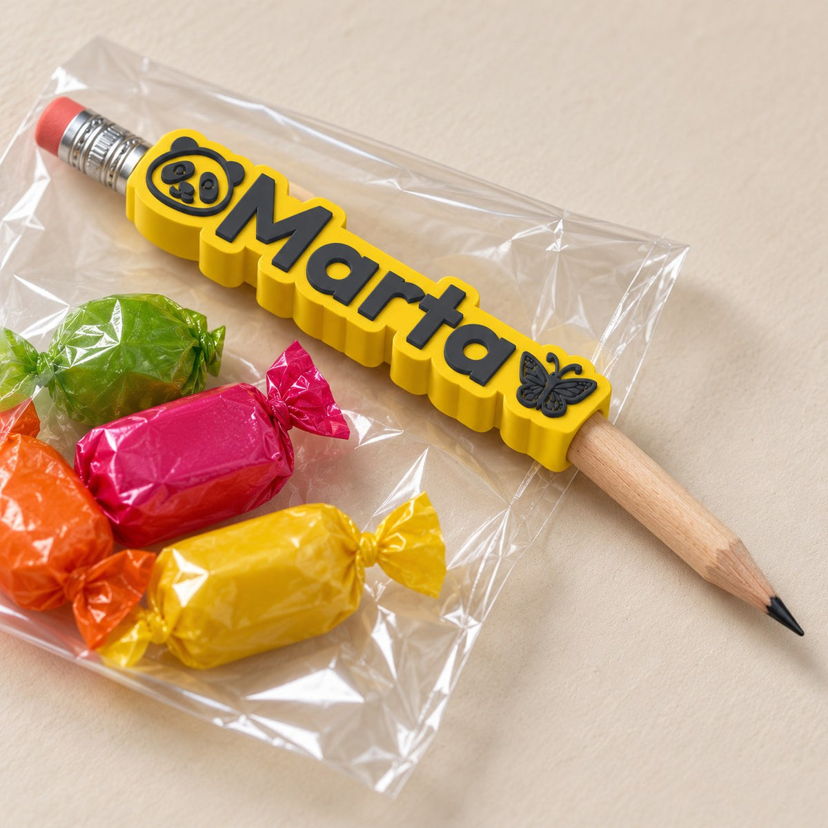 Emoji Name Pencil Topper: 'Marta' topper on a pencil in a party goody bag with a few sweets, on a light table