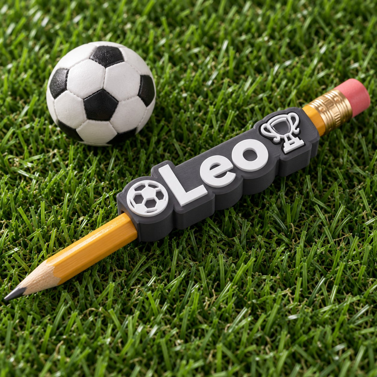 Football Name Pencil Topper: 'Leo' topper on a pencil next to a small football on artificial grass