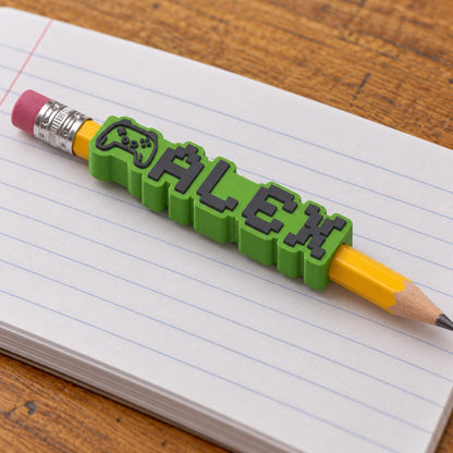 Gamer Name Pencil Topper: 'ALEX' topper on a yellow wooden pencil lying on an exercise book on a school desk
