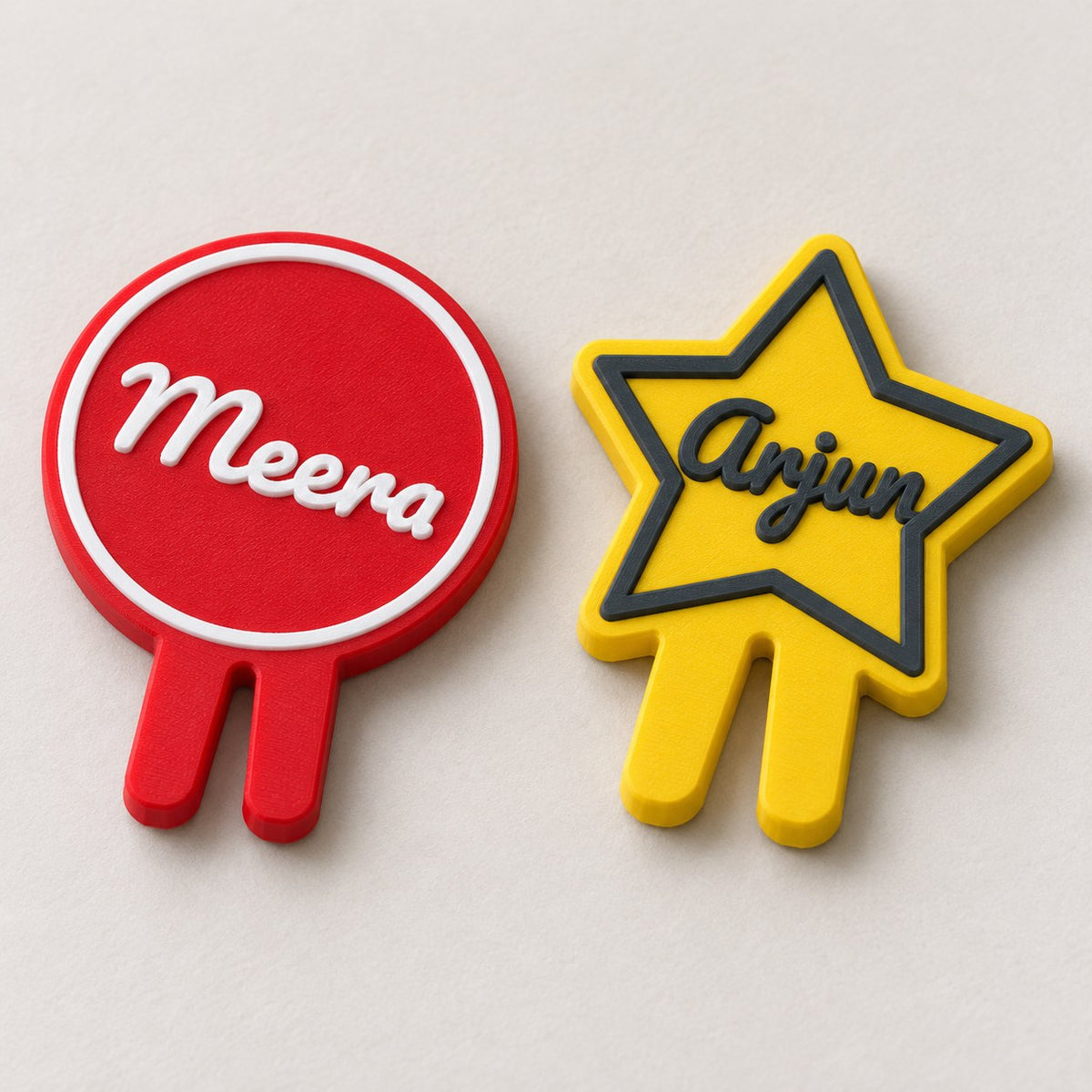 Glass Name Marker: red Meera circle and a yellow star-shaped Arjun marker lying flat side by side, top-down
