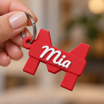 Initial and Name Banner Keychain: red 'Mia' keychain on a steel split ring held loosely by a woman's hand against a soft blurred background (hand allowed in this one only)
