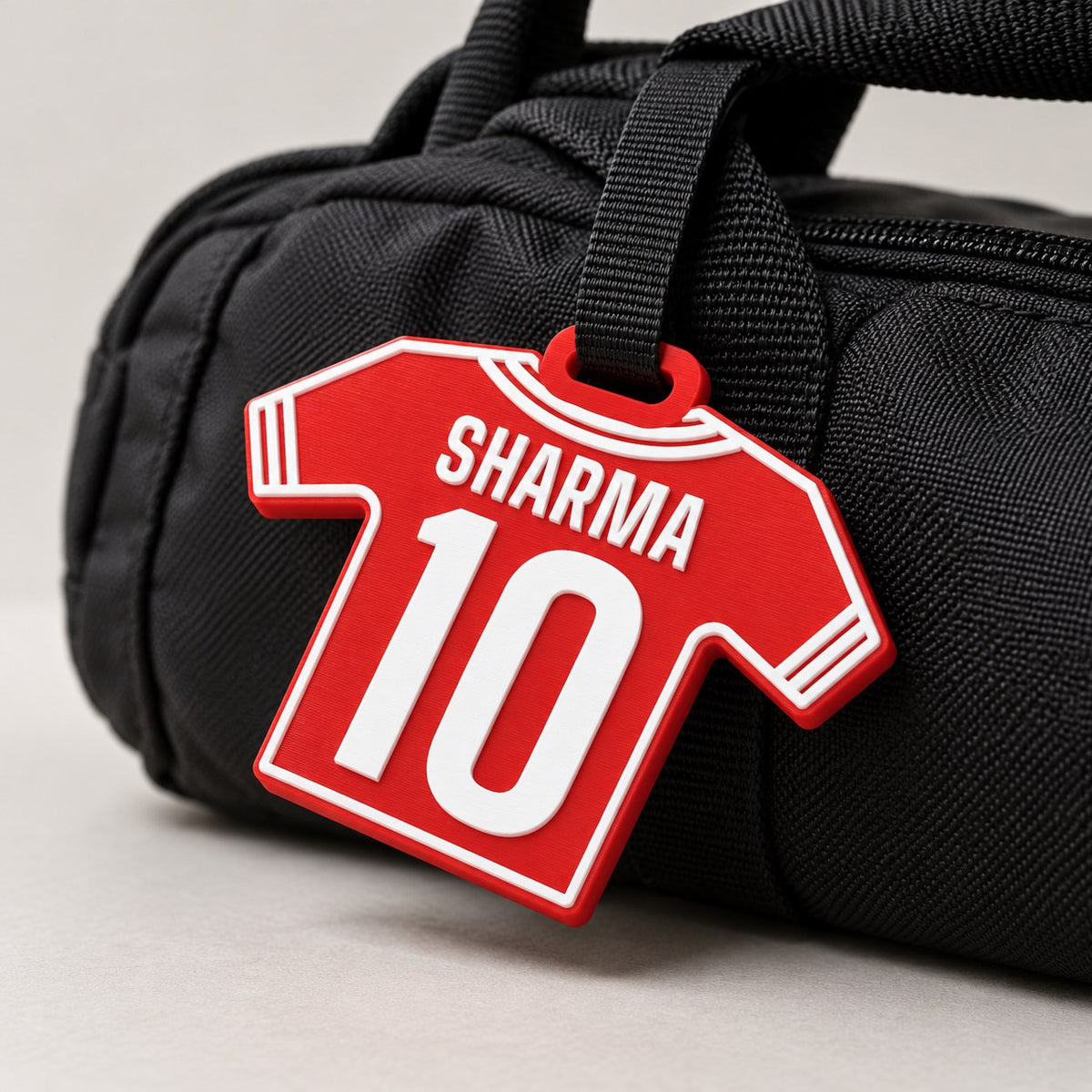 Jersey Kit Bag Tag: red 'SHARMA 10' tag hanging by a black strap from the handle of a black sports kit bag