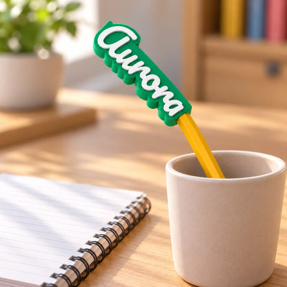 Name Pencil Topper: 'Aurora' topper on a yellow pencil standing in a simple pencil cup on a child's desk with a notebook, soft daylight