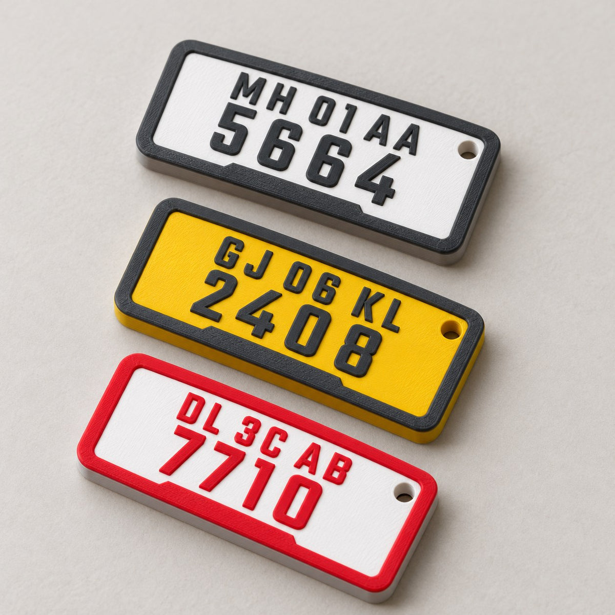 Number Plate Keychain: three plate keychains laid flat in a row, top-down at a slight angle, all registrations readable