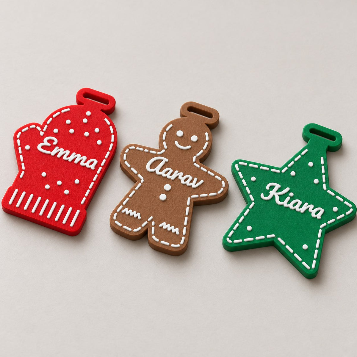 Personalised Christmas Ornament: three ornaments (red mitten Emma, brown gingerbread Aarav, green star Kiara) laid flat in a loose row, top-down at a slight angle