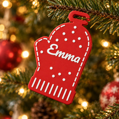 Personalised Christmas Ornament: red 'Emma' mitten hanging from a branch of a decorated Christmas tree with warm fairy lights out of focus