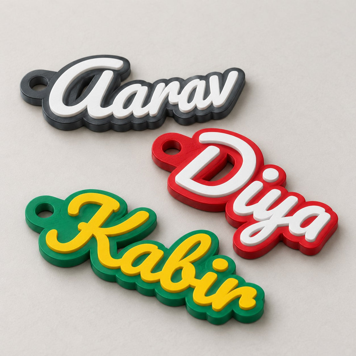 Personalised Name Keychain: three keychains (Aarav, Diya, Kabir) laid flat in a loose fan, top-down at a slight angle