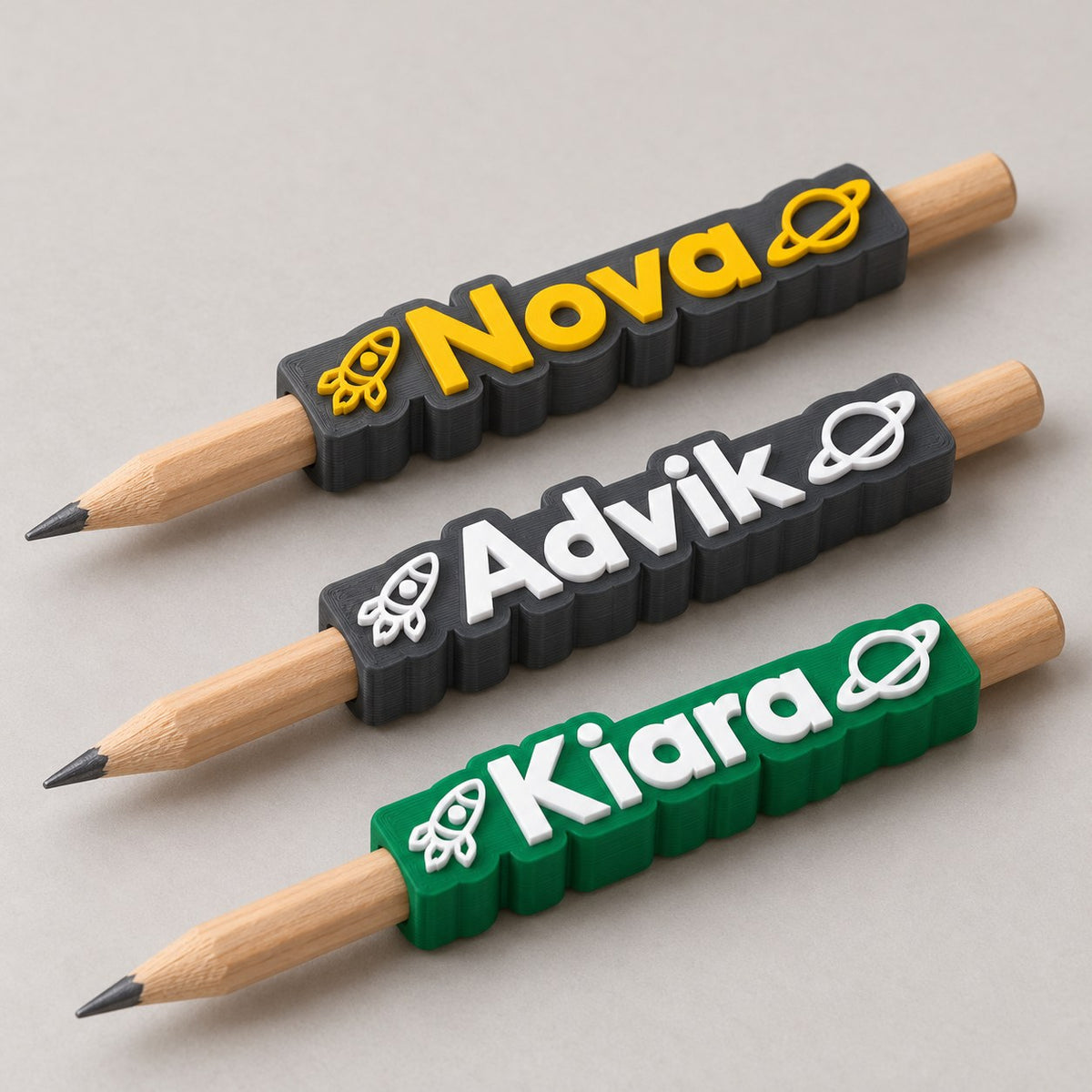 Space Name Pencil Topper: three toppers (Nova, Advik, Kiara) each on the top of a pencil, the pencils lying side by side