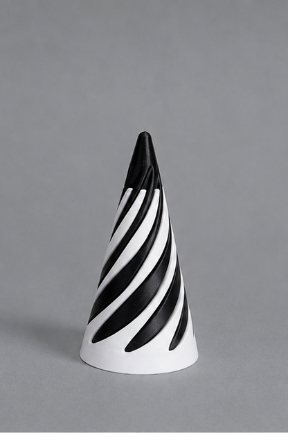 A modern cone-shaped decorative object featuring a bold black and white spiral stripe pattern, photographed against a solid gray studio background.