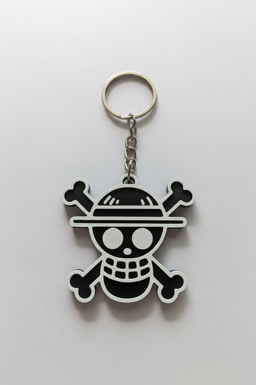 A One Piece Jolly Roger keychain featuring a black and white skull and crossbones design with a straw hat, attached to a silver metal split ring and chain, shown on a plain light background.