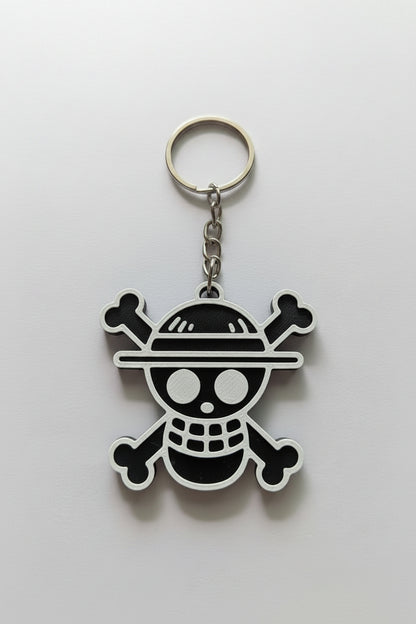 A One Piece Jolly Roger keychain featuring a black and white skull and crossbones design with a straw hat, attached to a silver metal split ring and chain, shown on a plain light background.