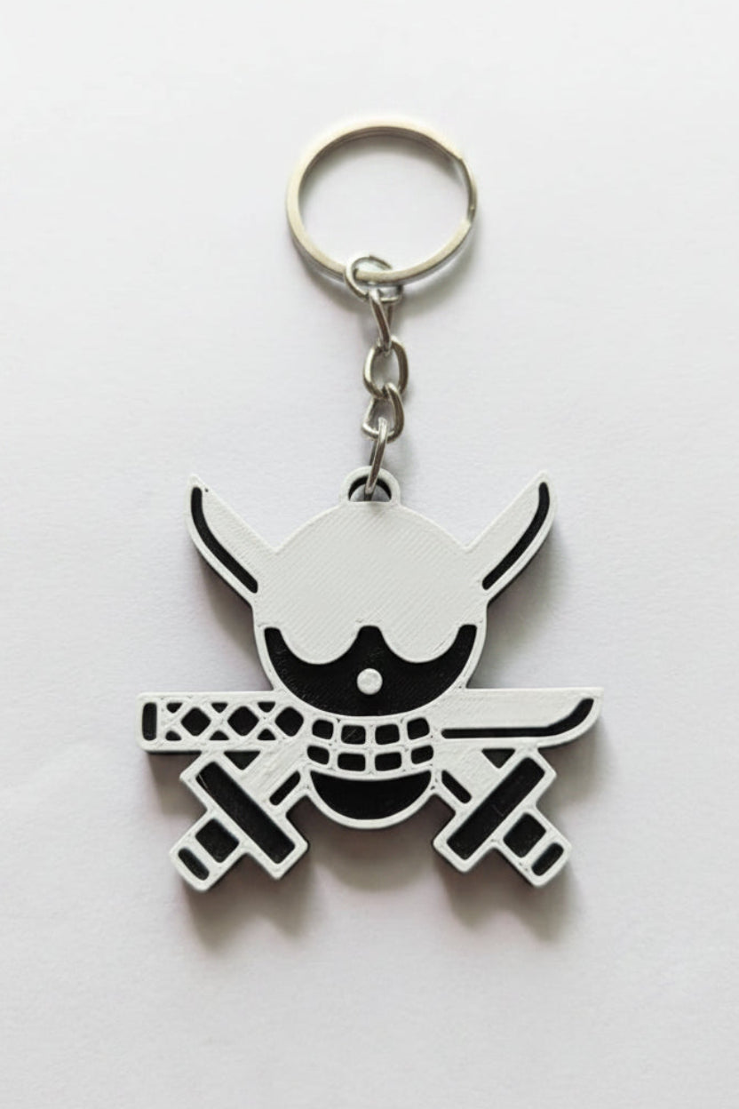 A silver metal keychain featuring a stylized skull and crossbones design with black and white details, resting on a plain light gray surface.