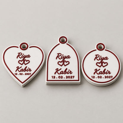 Wedding Favour Keychain: heart, Mughal arch and medallion versions side by side, laid flat, all with Riya, Kabir and the date
