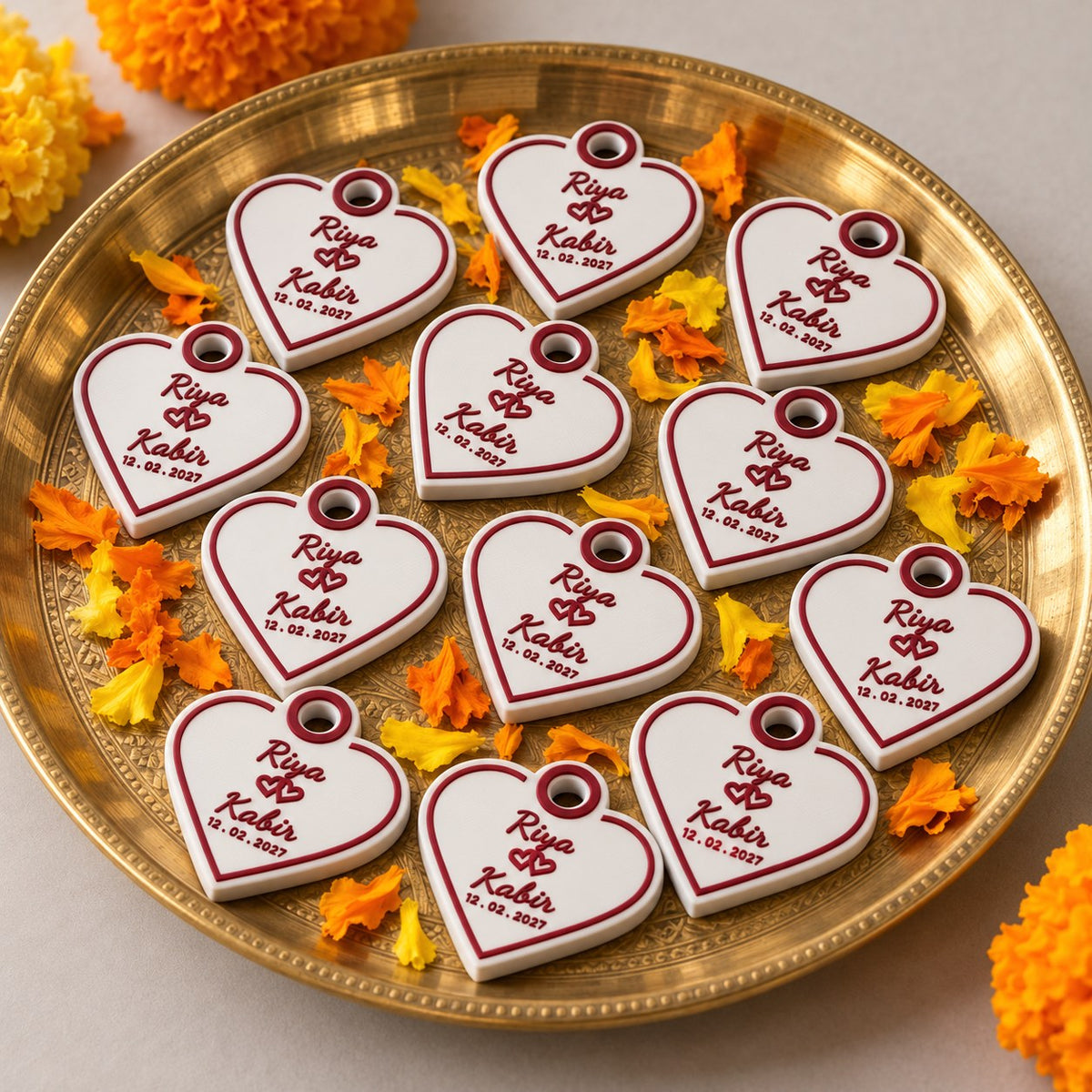 Wedding Favour Keychain: about a dozen identical heart keychains arranged on a brass thali with marigold petals around it, as wedding return gifts