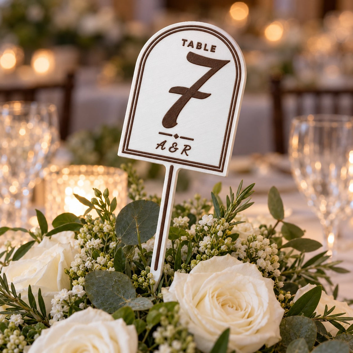 Wedding Table Number Stand: table 7 stand pushed into a centrepiece of white roses and greenery on a wedding table, natural evening light