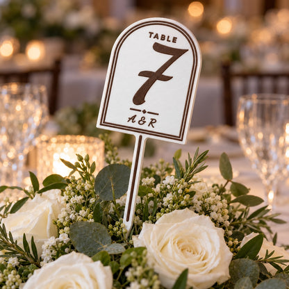 Wedding Table Number Stand: table 7 stand pushed into a centrepiece of white roses and greenery on a wedding table, natural evening light