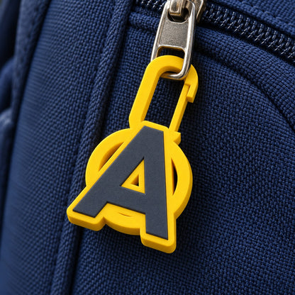 Yellow initial A zip charm clipped to the zip pull of a navy school backpack